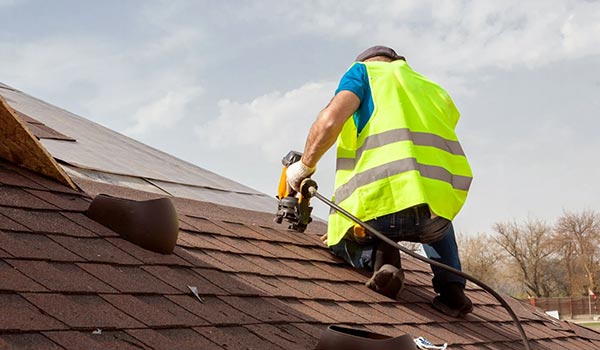 man using nail gun on roof shingles