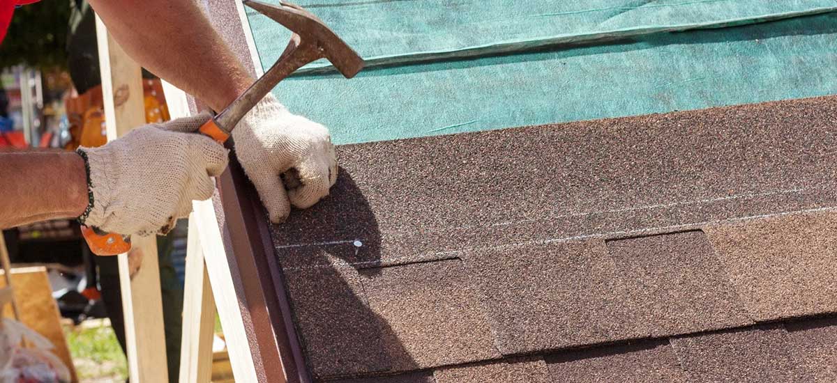 hammering nails into shingles on roof